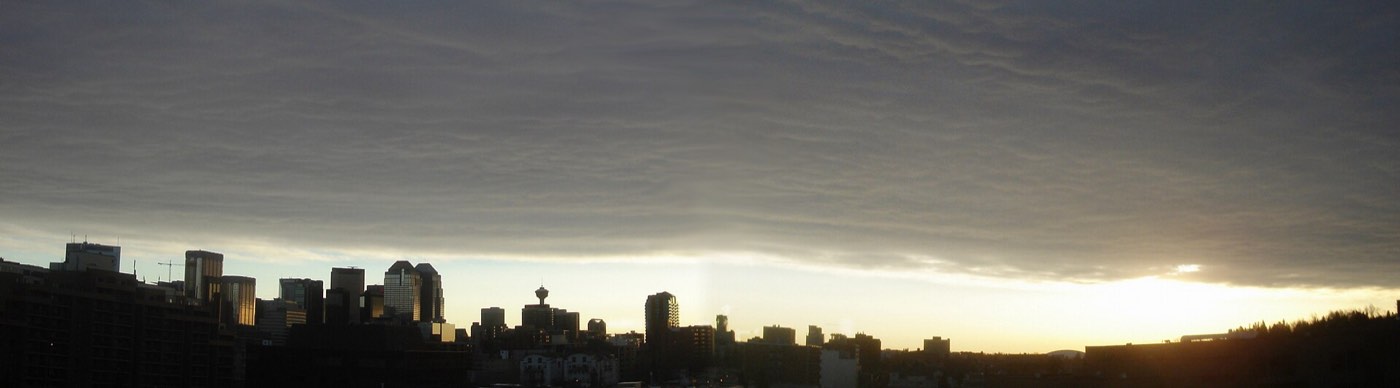 A chinook arch — a long band of cloud with clear sky beneath it — over the Calgary skyline at sunset