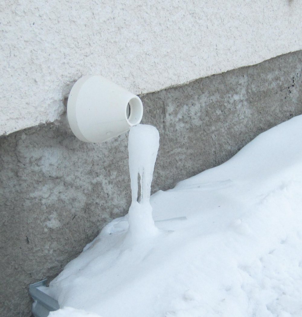 The plastic exhaust outlet of a condensing furnace on an outside wall, with frozen condensate hanging from it into a snowbank