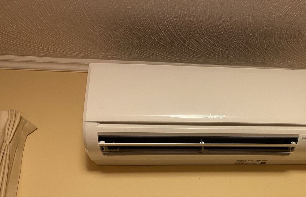 The wall-mounted indoor head of a ductless heat pump above a window in a living room
