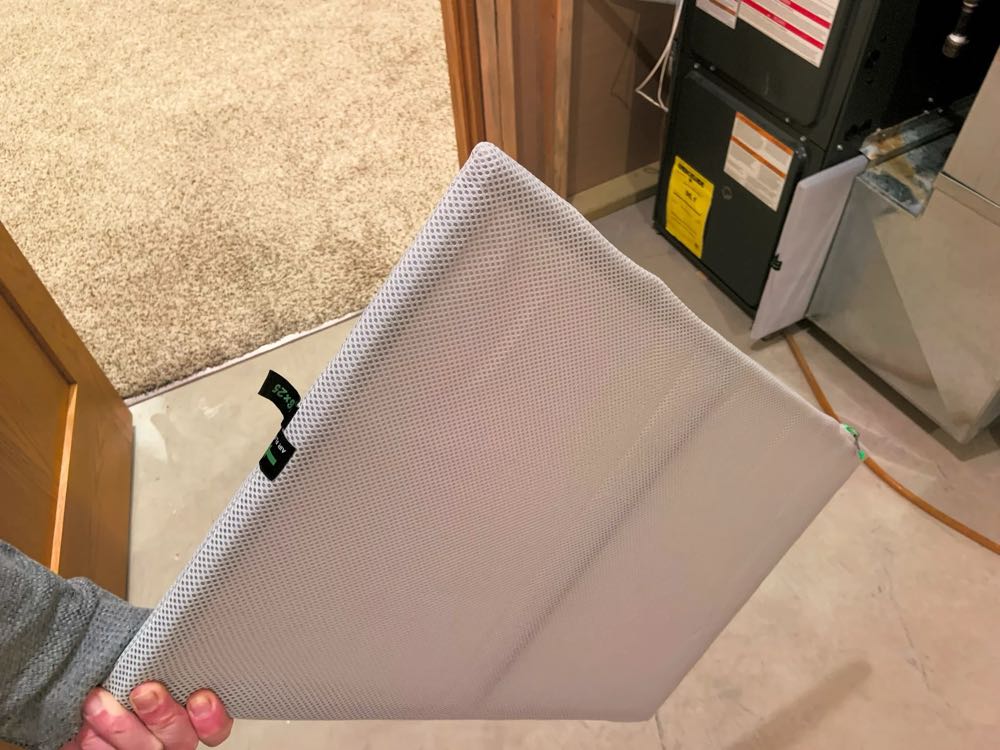 A hand holding a furnace air filter pulled from the slot of a gas furnace in a basement utility room